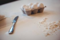 Egg in carton knife and flour on kitchen worktop at home — Stock Photo