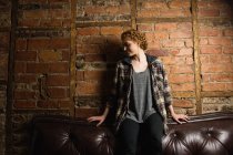 Bella donna seduta sul divano contro muro di mattoni — Foto stock