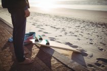 Section basse de l'homme avec planche de surf debout sur la plage — Photo de stock