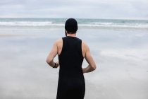 Rear view of man in swimming costume and swimming cap running on beach — Stock Photo