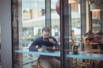 Чоловік виконавчий використовує мобільний телефон, маючи каву в кафетерії — стокове фото