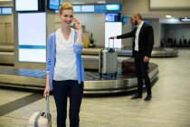 Бізнес-леді стоячи з багажем говорити на мобільний телефон у зону очікування в аеропорту терміналу — стокове фото