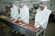 Мужчины-мясники режут мясо на мясокомбинате — стоковое фото