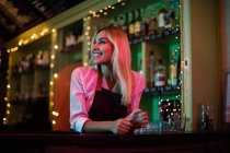 Hermosa camarera sonriente inclinada en el mostrador del bar - foto de stock