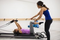 Женщина-тренер помогает женщине с упражнениями на растяжку на реформаторе в тренажерном зале — стоковое фото