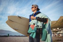 Homem carregando prancha de surf em pé na praia — Fotografia de Stock