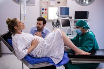 Médico examinando mulher grávida durante o parto, enquanto o homem segurando a mão na sala de cirurgia — Fotografia de Stock