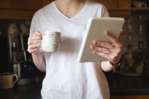 Metà sezione della donna che utilizza tablet digitale mentre prende il caffè in cucina a casa — Foto stock