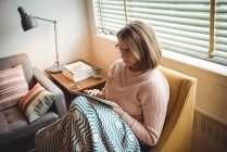 Frau sitzt mit digitalem Tablet im heimischen Wohnzimmer auf Stuhl — Stockfoto