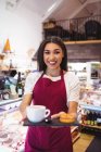 Portrait de serveuse souriante tenant une tasse de café et des collations au supermarché — Photo de stock