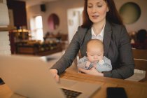 Мама использует ноутбук, держа новорожденного ребенка дома — стоковое фото