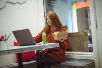 Рыжая женщина использует ноутбук во время еды салата — стоковое фото