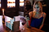 Femme utilisant un téléphone portable avec du vin rouge sur la table au bar — Photo de stock