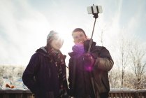 Felice coppia di sciatori cliccando su un selfie con bastone selfie nella stazione sciistica — Foto stock