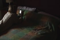 Жінка лежить і використовує мобільний телефон на ліжку в спальні — стокове фото