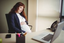 Беременная деловая женщина, трогающая живот в офисе — стоковое фото