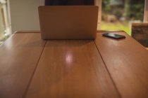 Laptop e telefone celular na mesa de madeira em casa — Fotografia de Stock