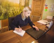 Frau benutzt Laptop und schreibt im Büro auf Notizblock — Stockfoto