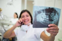 Dentist checking x-ray report while talking on mobile phone at aesthetic clinic — Stock Photo
