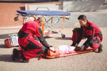 Les ambulanciers mettent la fille blessée sur une planche arrière dans la rue — Photo de stock