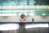 Empresaria que usa laptop mientras toma café en la sala de espera en la terminal del aeropuerto - foto de stock