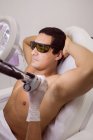 Médico realizando depilación láser en la piel de la axila del paciente masculino en la clínica - foto de stock