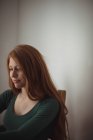 Redhead woman sitting indoors and looking down — Stock Photo