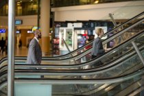 Gente de negocios con equipaje de pie en escaleras mecánicas en la terminal del aeropuerto - foto de stock