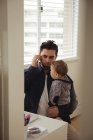 Pai falando no celular enquanto segurava seu bebê em casa — Fotografia de Stock