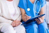 Midsection of doctor writing on clipboard in clinic — Stock Photo