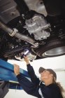 Mecánica femenina examinando un coche con linterna en garaje de reparación - foto de stock