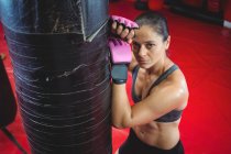 Female boxer leaning on punching bag in fitness studio — Stock Photo