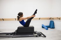 Femme faisant de l'exercice sur le réformateur dans la salle de gym en posture d'étirement — Photo de stock