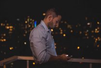 Чоловік використовує свій мобільний телефон на балконі вночі — стокове фото