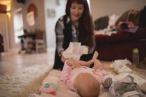 Mère changeant la couche de bébé dans le salon à la maison — Photo de stock