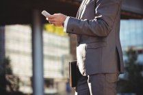 Partie médiane d'un homme d'affaires utilisant un téléphone portable près d'un immeuble de bureaux — Photo de stock