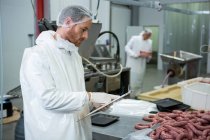 Boucher mâle tenant des dossiers sur presse-papiers à l'usine de viande — Photo de stock