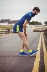 Athlete performing stretching exercise on road — Stock Photo