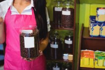 Sezione media di negoziante femminile che tiene il vaso di chicchi di caffè al banco in negozio — Foto stock
