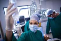Cirurgião feminino ajustando iv gotejamento no teatro de operação do hospital — Fotografia de Stock