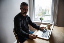 Mann benutzt Laptop und Handy im heimischen Wohnzimmer — Stockfoto