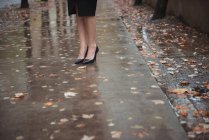 Feet in stylish shoes of businesswoman on wet pedestrian walkway — Stock Photo