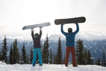 Rear view of man and woman holding snowboard at mountain during winter against sky — Stock Photo