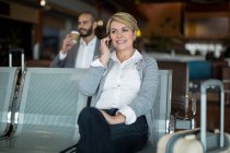 Smiling businesswoman talking on mobile phone in waiting area at airport terminal — Stock Photo