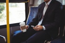 Бізнесмен тримає одноразову чашку кави і використовує мобільний телефон в автобусі — стокове фото