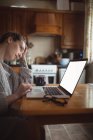 Tensed woman using laptop on table in kitchen at home — Stock Photo