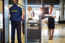 Airport security guard with passengers walking through body scanner at airport terminal — Stock Photo