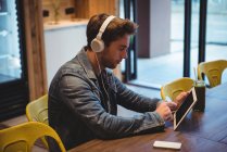 Чоловік слухає музику з навушниками під час використання цифрового планшета в кафе — стокове фото