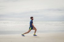 Спортсмен, що виконує розтягування вправи на піщаному пляжі — стокове фото