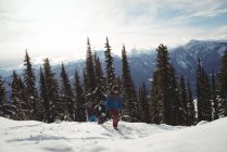 Casal correndo na montanha coberta de neve contra árvores — Fotografia de Stock